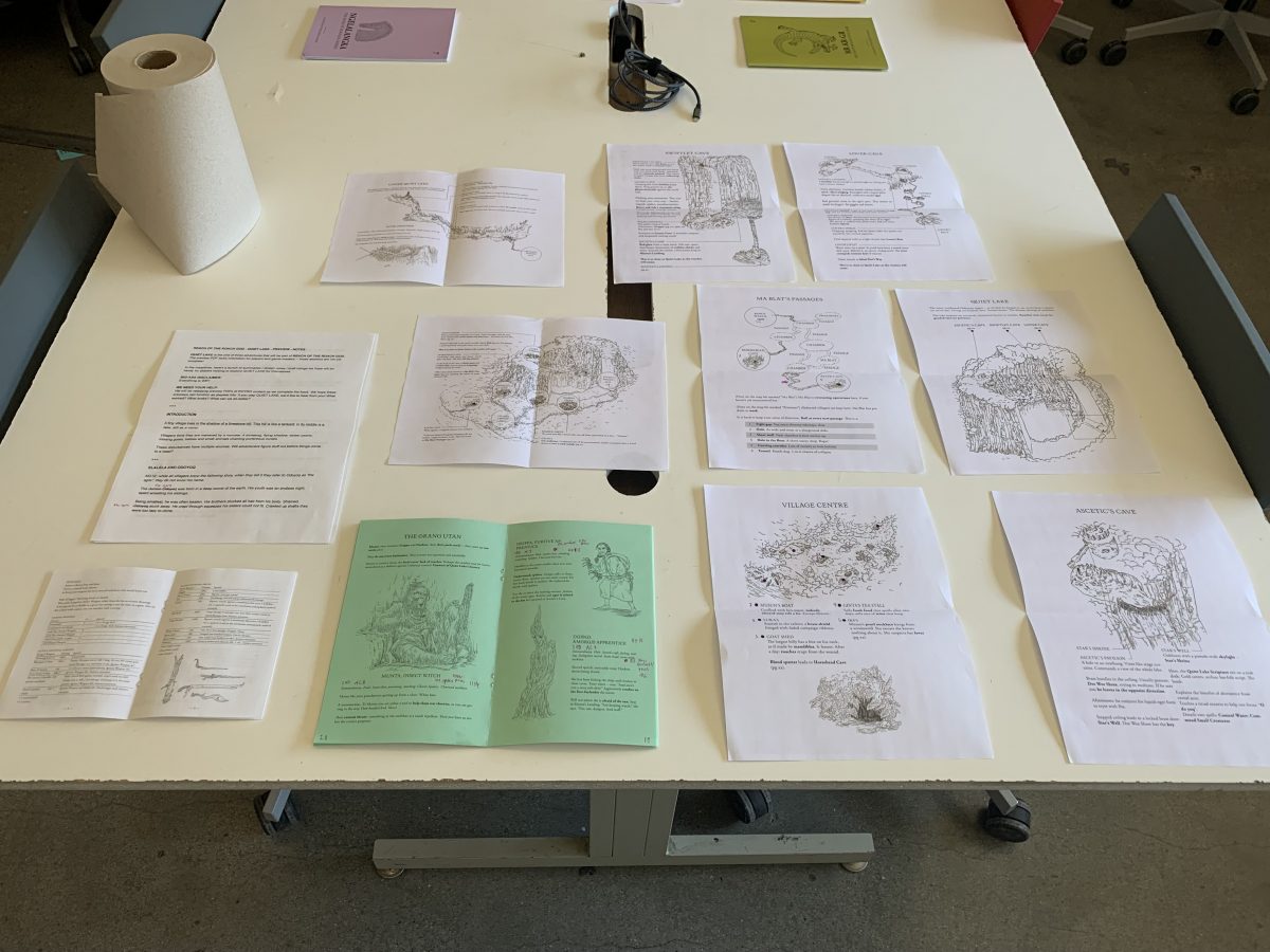 Printed materials from Quiet Lake laid out on a table. There are many maps, a printed zine of the adventure, and a printed zine of the ruleset